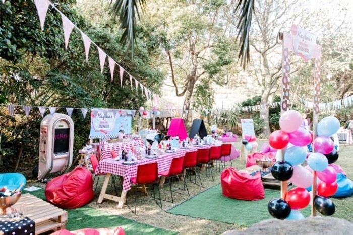  Red plastic chairs with steel frames and wooden tables with red and white table cloths.